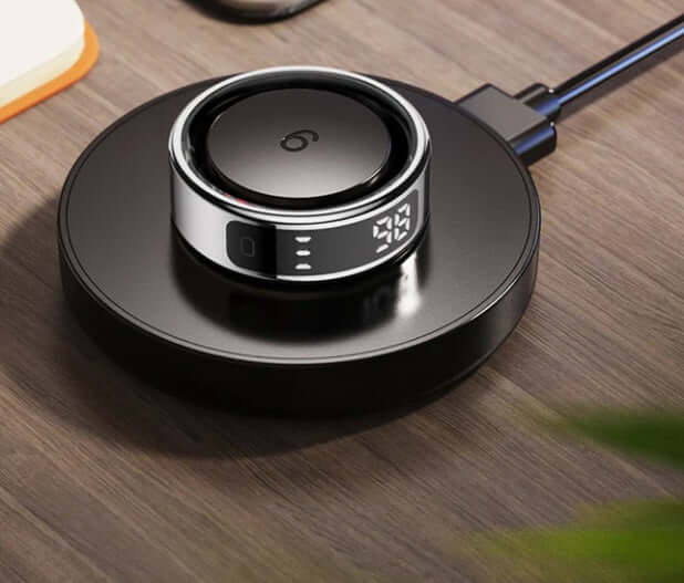 Colmi R12 Smart Ring - Gold wirelessly charging on a sleek black charging dock with digital display.