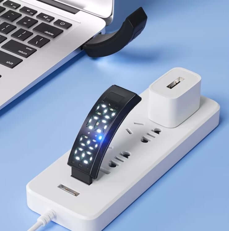 Polaristech Smart bracelet charging on a power strip beside a laptop, showcasing its LED display and design.